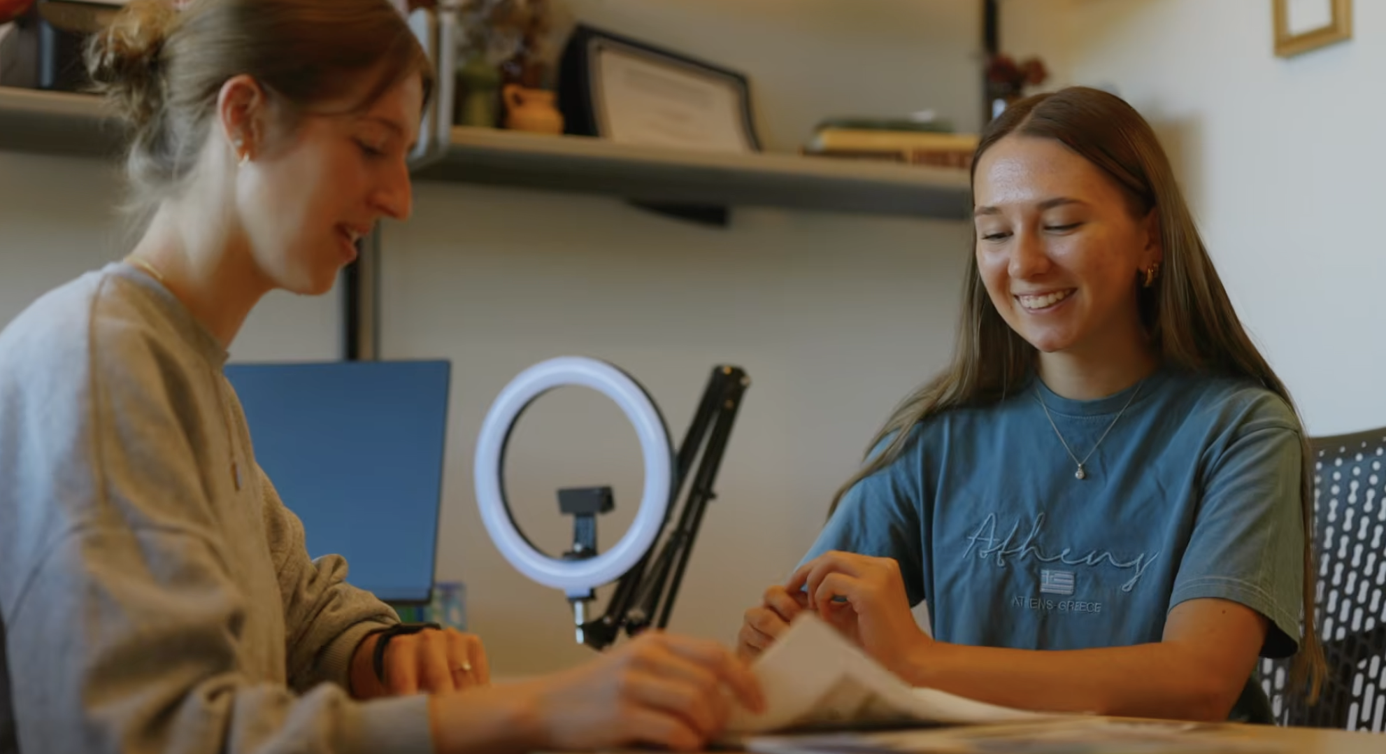 Two students collaborate on a project at a desk in a workspace, smiling as they review materials together.